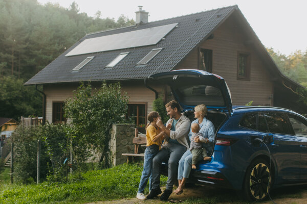 Family with electric car standing in front their house with solar panels on the roof. Solar energy and sustainable lifestyle of young family. Concept of green energy and sustainable future for next generations.