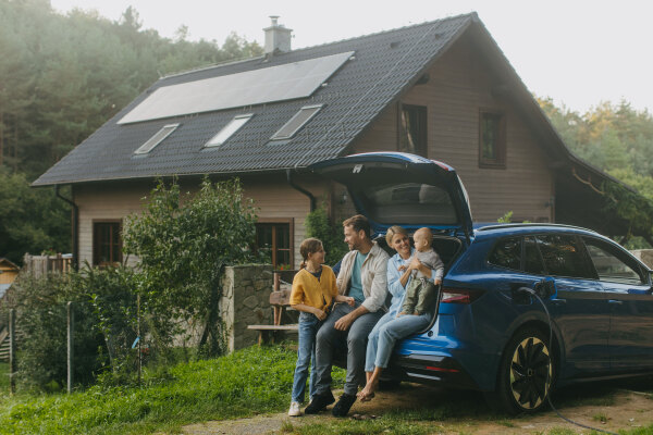 Family with electric car standing in front their house with solar panels on the roof. Solar energy and sustainable lifestyle of young family. Concept of green energy and sustainable future for next generations.