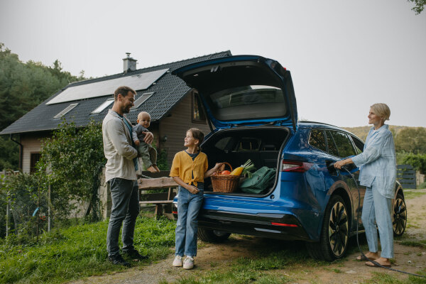 Beautiful family with electric car in front house with solar panels on roof. Solar, green energy and sustainable lifestyle of young family.