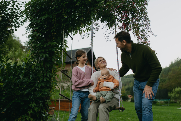 Beautiful family swinging on a swing in the garden, having fun and spending quality time together outdoors during a warm autumn day.