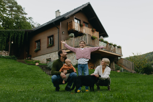 Family standing in front their house with solar panels on the roof. Solar energy and sustainable lifestyle of young family. Concept of green energy and sustainable future for next generations.