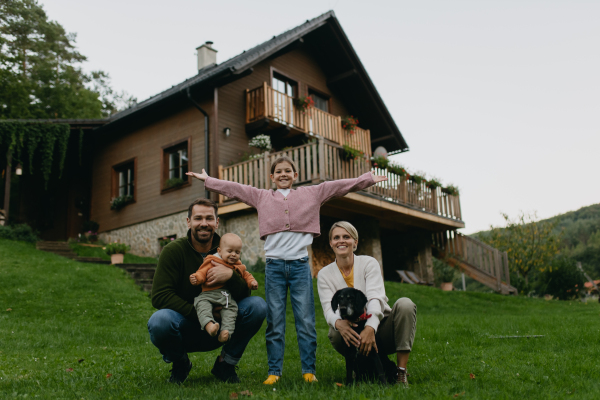 Family standing in front their house with solar panels on the roof. Solar energy and sustainable lifestyle of young family. Concept of green energy and sustainable future for next generations.