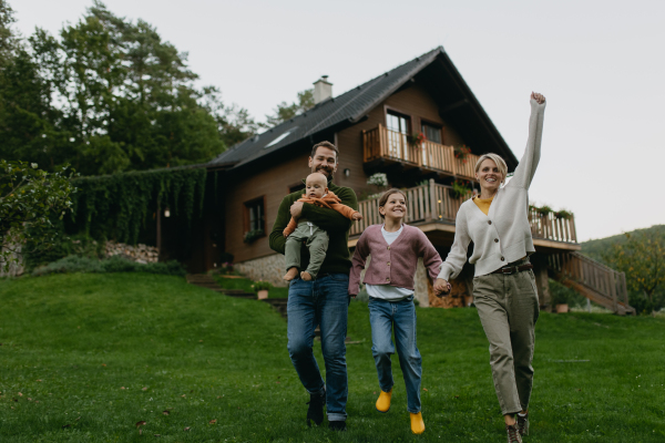 Family standing in front their house with solar panels on the roof. Solar energy and sustainable lifestyle of young family. Concept of green energy and sustainable future for next generations.