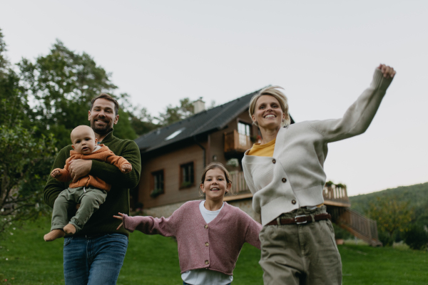 Family standing in front their house with solar panels on the roof. Solar energy and sustainable lifestyle of young family. Concept of green energy and sustainable future for next generations.