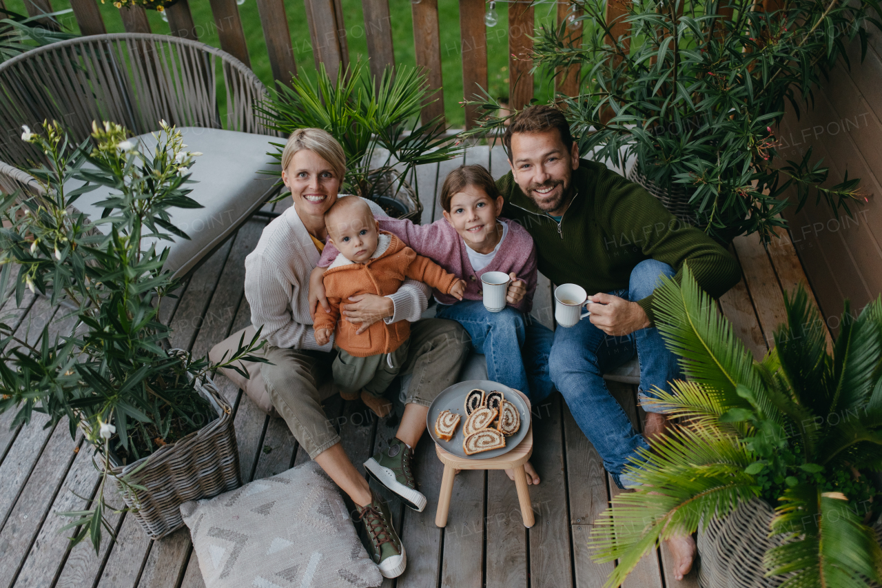 Top view of family having a snack outdoors in the garden patio, drinking warm tea and eating sweet roll bread. Hygge family autumn time.