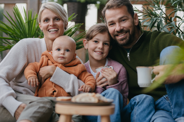 Portrait of family sitting outdoors in the garden patio. Drinking warm tea and eating sweet roll bread. Hygge family autumn time.