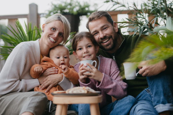 Portrait of family sitting outdoors in the garden patio. Drinking warm tea and eating sweet roll bread. Hygge family autumn time.