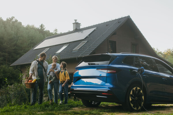 Family with electric car standing in front their house with solar panels on the roof. Solar energy and sustainable lifestyle of young family. Concept of green energy and sustainable future for next generations.