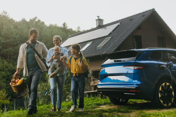 Beautiful family with electric car in front house with solar panels on roof. Solar, green energy and sustainable lifestyle of young family.