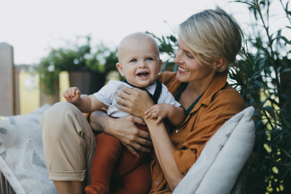 Beatiful mother sitting with her little son outdoors, in the garden patio. Warm autumn day of mother with toddler. Hygge motherhood.