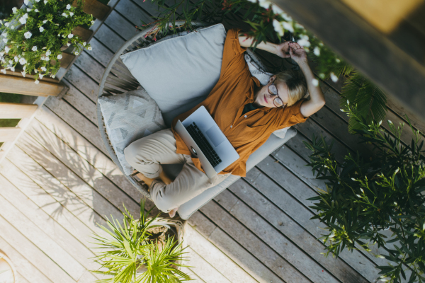 Top view of woman working outdoors in the garden, with laptop on legs. Working mother having break, thinking about new business or creative idea.