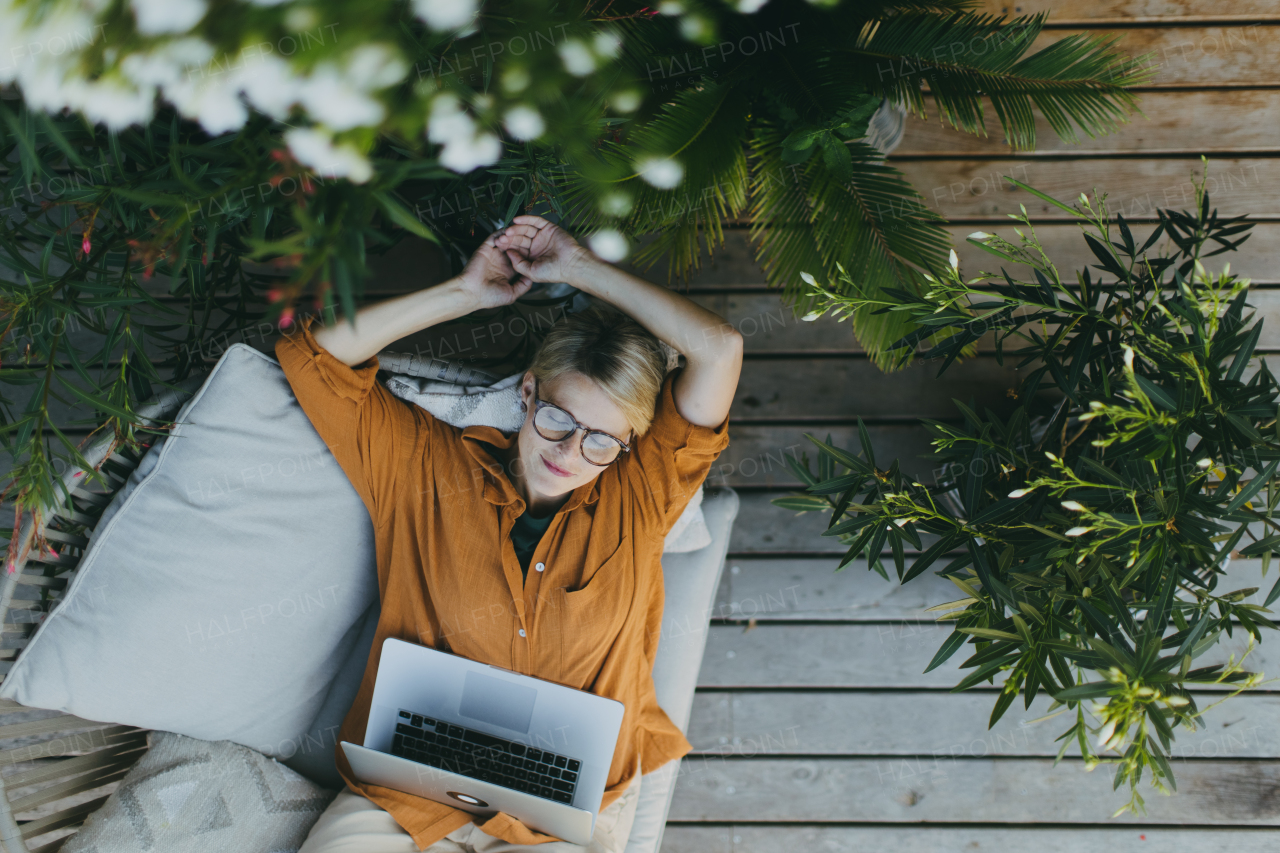 Top view of woman working outdoors in the garden, with laptop on legs. Working mother having break, thinking about new business or creative idea. Concept of outdoor home office.