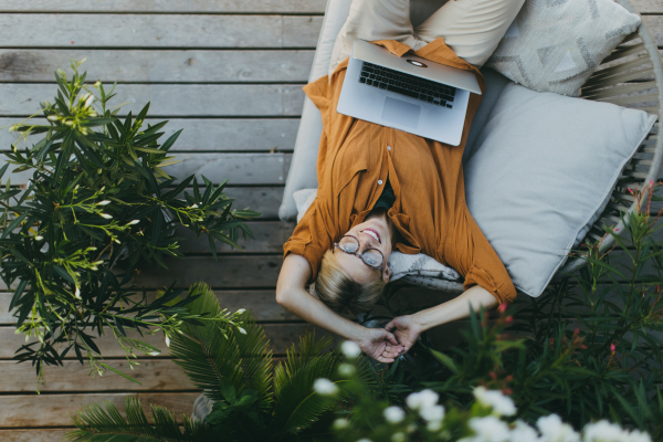 Top view of woman working outdoors in the garden, with laptop on legs. Working mother having break, thinking about new business or creative idea.