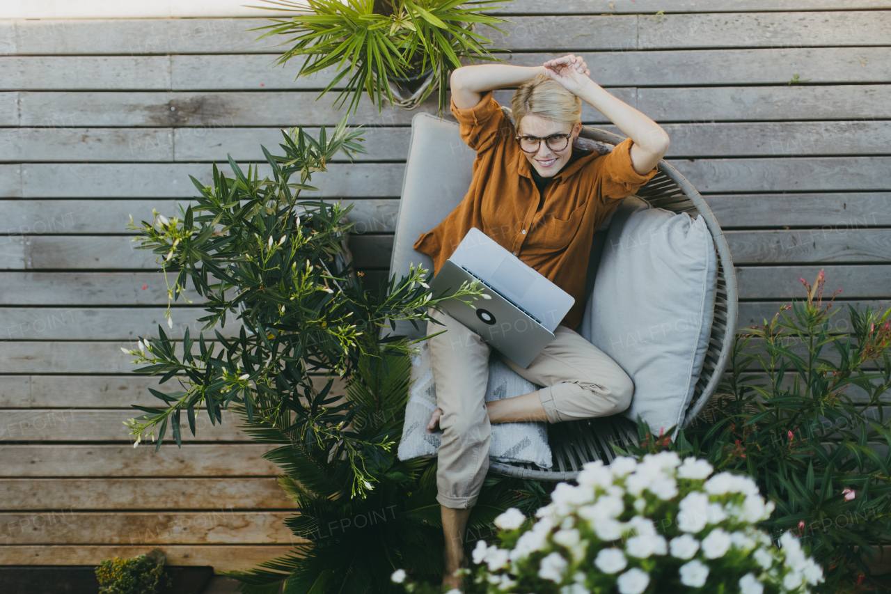 Top view of woman working outdoors in the garden, with laptop on legs. Working mother having break, thinking about new business or creative idea.