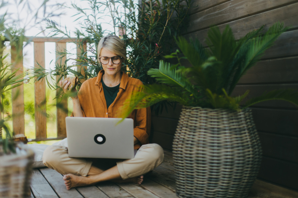 Woman working on laptop while eating sandwich. Businesswoman working remotely from outdoor homeoffice, having light lunch in garden. Concept of outdoor home office.