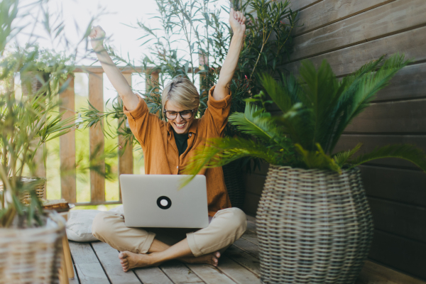 Woman working in garden, , with laptop on legs, celebrating success Businesswoman working remotely from outdoor homeoffice. Concept of outdoor home office.