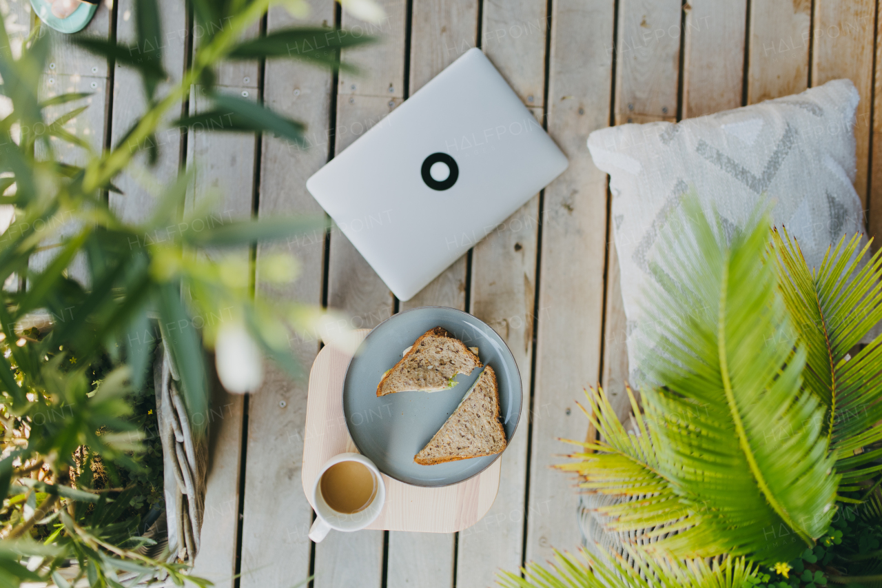 Top view of outdoor garden patio setting with notebook, plate with light lunch and cup of coffee. Simple outdoor home office setting for remote employee, telecommuter.