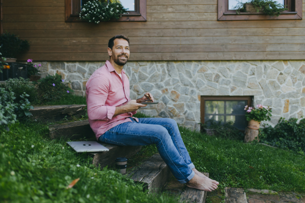 Low angle shot of man working outdoors in the garden, eating lunch or snack, sandwich.Businessman working remotely from homeoffice, thinking about new business or creative idea.