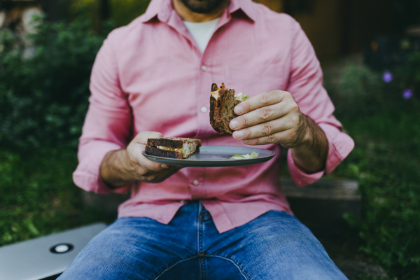 Close up of man working outdoors in the garden, eating lunch or snack, sandwich. Businessman working remotely from homeoffice, thinking about new business or creative idea.