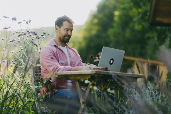 Low angle shot of man working outdoors in the garden, with laptop on his legs. Businessman working remotely from homeoffice, thinking about new business or creative idea.