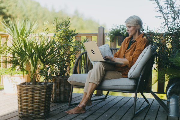 Woman working in garden, with laptop on legs. Businesswoman working remotely from the outdoor homeoffice, eating light lunch, sandwich. Concept of outdoor home office.