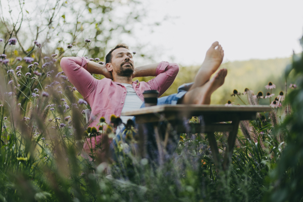 Relaxed barefoot man sitting in the garden with feet up on the table. Father having moment to himself while his kids are in school.