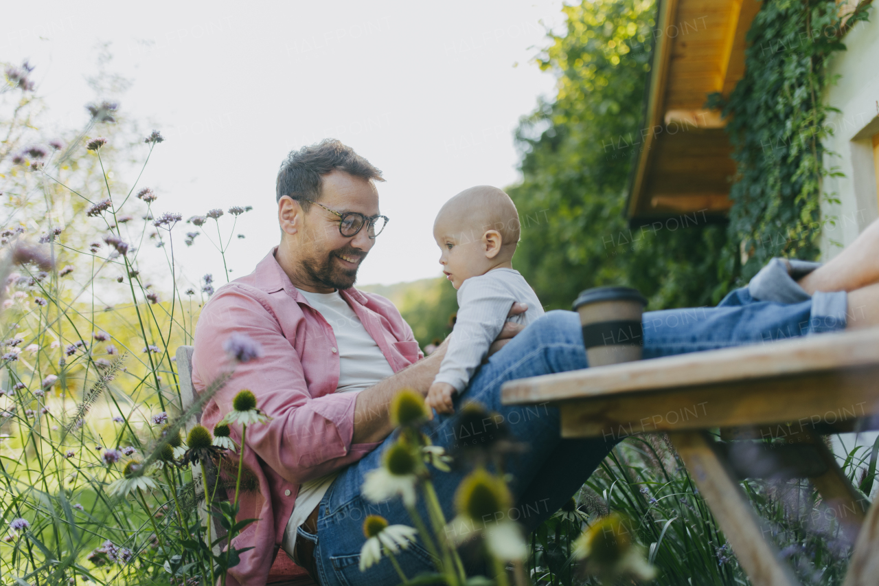 Man sitting in the garden with feet on table, playing with his baby son. Father having bonding moment with his little cute kid.