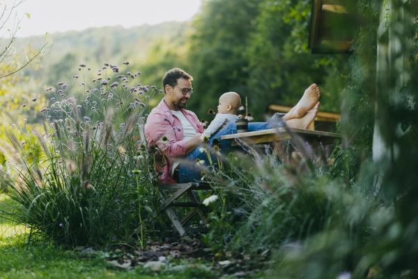 Man sitting in the garden with feet on table, playing with his baby son. Father having bonding moment with his little kid.