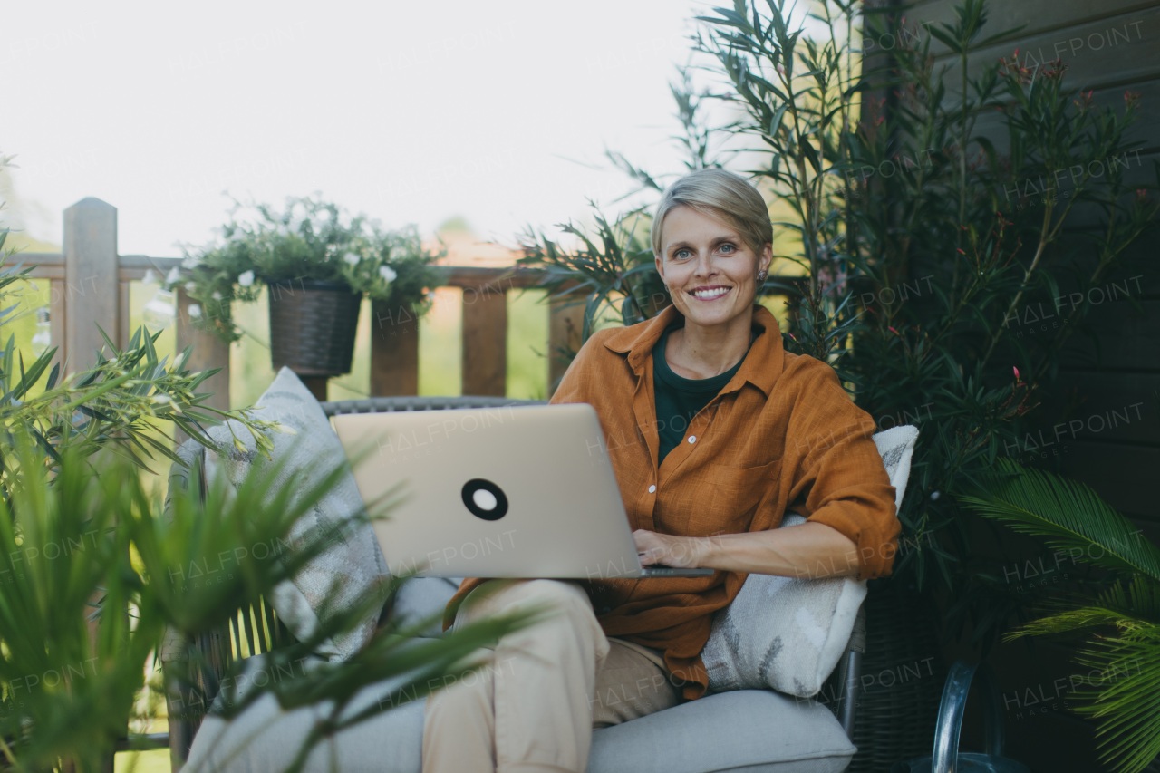 Woman working in garden, with laptop on legs. Businesswoman working remotely from outdoor homeoffice, thinking about new business or creative idea. Concept of outdoor home office.