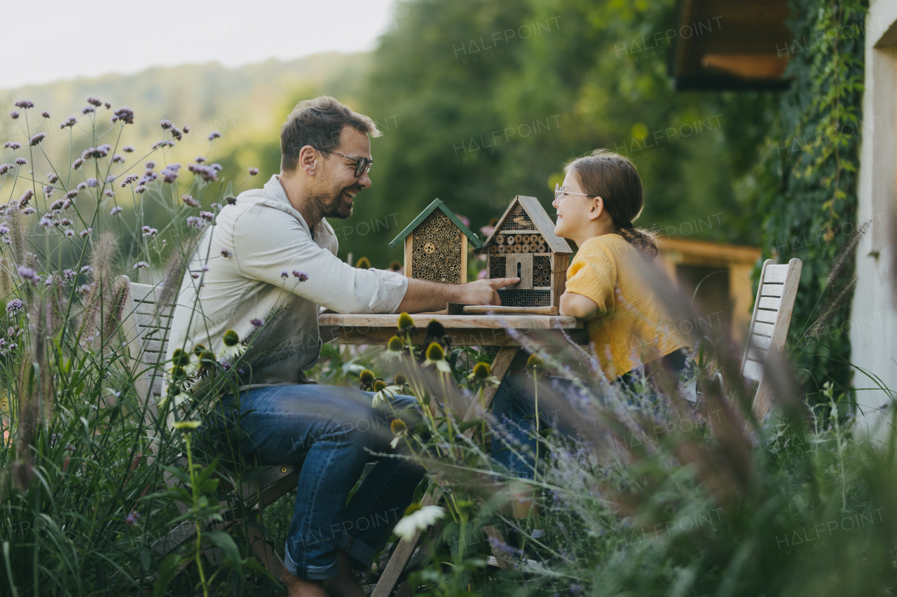 Father with daughter making an bug hotel, or insect house outdoors in the garden. Girl learning about insects, garden ecosystem and biodiversity.