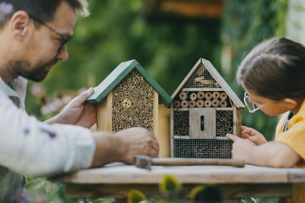 Father with daughter making an bug hotel, or insect house outdoors in the garden. Girl learning about insects, garden ecosystem and biodiversity.