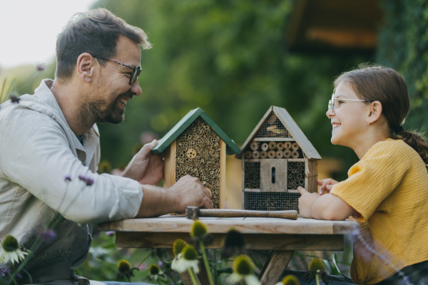 Father with daughter making an bug hotel, or insect house outdoors in the garden. Girl learning about insects, garden ecosystem and biodiversity.