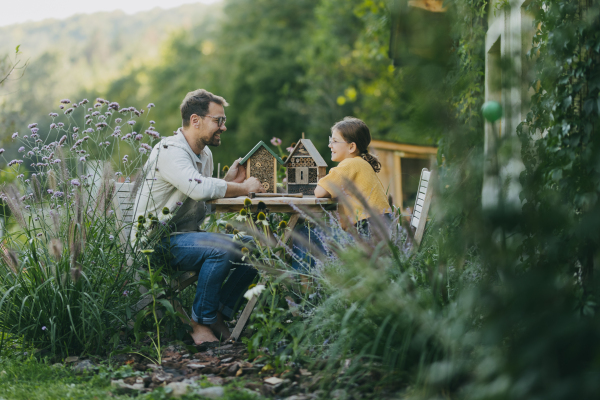 Father with daughter making an bug hotel, or insect house outdoors in the garden. Girl learning about insects, garden ecosystem and biodiversity.