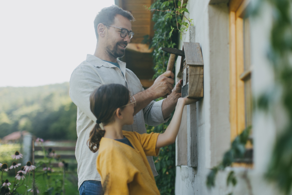 Father with daughter making an bug hotel, or insect house outdoors in the garden. Girl learning about insects, garden ecosystem and biodiversity.