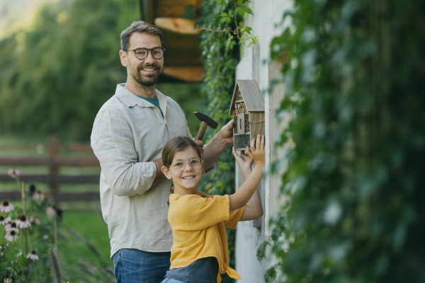 Father with daughter making an bug hotel, or insect house outdoors in the garden. Girl learning about insects, garden ecosystem and biodiversity.