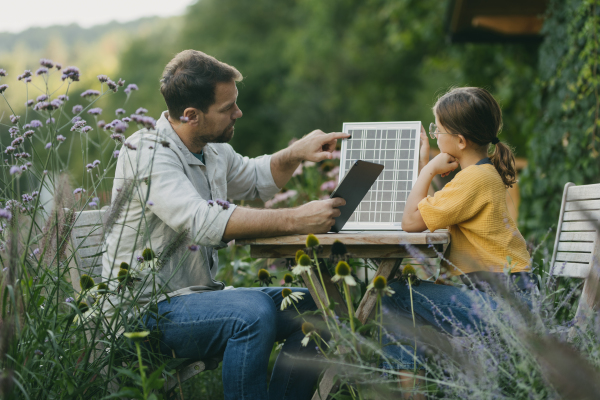 Father teaching daughter about solar panels, photovoltaic, showing her results on tablet Solar energy and sustainable lifestyle of young family. Concept of green energy and sustainable future for next generations.