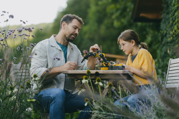 Young girl assembling a simple robot, father helping her. Father supporting daughter in pursuing robotics, science, IT technologies and programming.