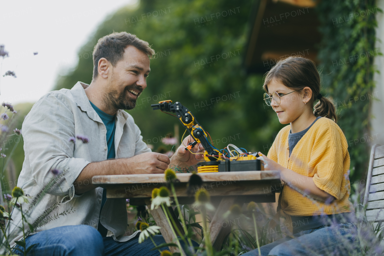 Young girl assembling a simple robot, father helping her. Father supporting daughter in pursuing robotics, science, IT technologies and programming. Concept of young girls in science.