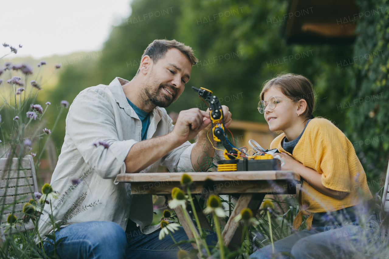 Young girl assembling a simple robot, father helping her. Father supporting daughter in pursuing robotics, science, IT technologies and programming.