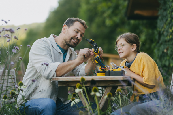 Young girl assembling a simple robot, father helping her. Father supporting daughter in pursuing robotics, science, IT technologies and programming.