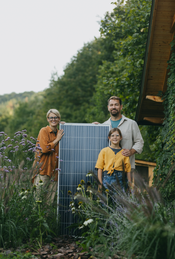 Father mother and daughter standing in garden holding solar panel. Solar energy and sustainable lifestyle of young family. Concept of green energy and sustainable future for next generations.