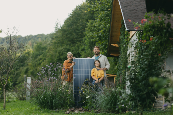 Father mother and daughter standing in garden holding solar panel. Solar energy and sustainable lifestyle of young family. Concept of green energy and sustainable future for next generations.