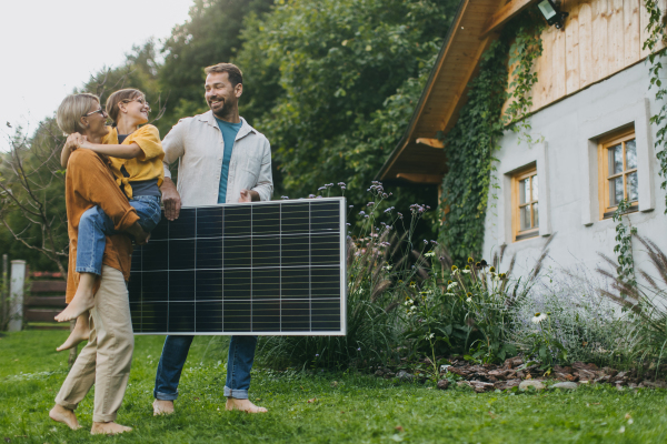 Father mother and daughter standing in garden holding solar panel. Solar energy and sustainable lifestyle of young family. Concept of green energy and sustainable future for next generations.