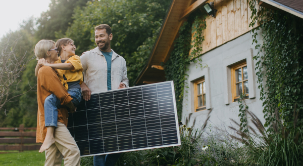 Family walking in garden holding solar panel. Solar energy and sustainable lifestyle of the young family. Concept of green energy and sustainable future for next generations.