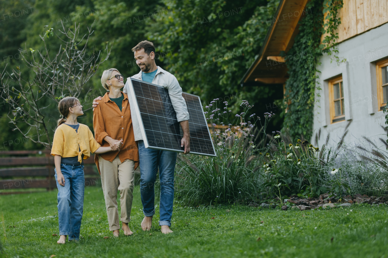 Father mother and daughter walking in garden holding solar panel. Solar energy and sustainable lifestyle of young family. Concept of green energy and sustainable future for next generations.