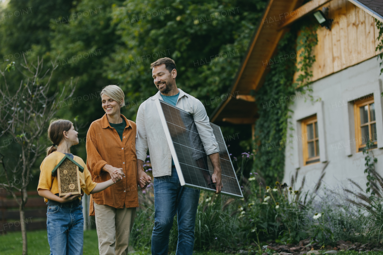 Family walking in garden holding solar panel. Solar energy and sustainable lifestyle of the young family. Concept of green energy and sustainable future for next generations.