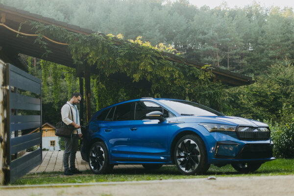 Portrait of a man charging his electric car in front of his house, plugging the charger into the charging port. The man is unplugging the charger from the fully charged car before going to the office.