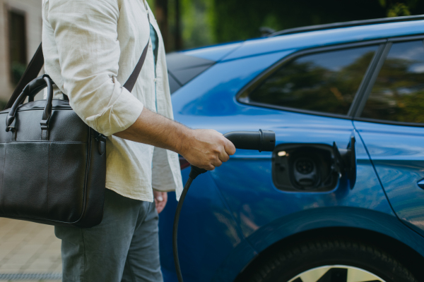 Close up of businessman charging his electric car in front of his house. Pluging charger in charging port.