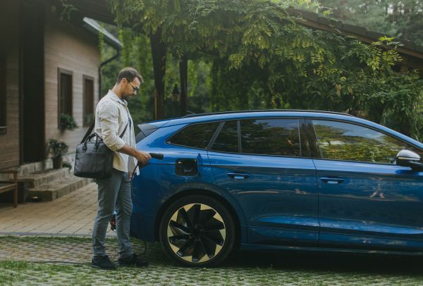 Portrait of businessman charging his electric car in front of his house. Pluging charger in charging port.