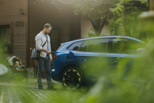 Portrait of a man charging his electric car in front of his house, plugging the charger into the charging port. The man is unplugging the charger from the fully charged car before going to the office.